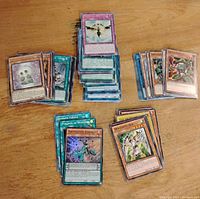 Stacks of holographic Yu-Gi-Oh! cards arranged on a wooden surface showing several identifiable cards and mixed card types.
