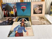 Group photo of 7 vinyl record albums on table, variety of artists including Air Supply and Carly Simon
