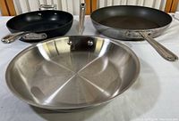 Photo showing three frying pans: 12-inch stainless steel, 10-inch black nonstick, 13-inch stainless steel with riveted handles