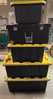 Stacked view of five black plastic storage containers with yellow lids showing varying sizes and sturdy construction.