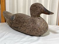 Full side view of the hand carved wood duck decoy on a white cloth surface, showing the entire body and head with painted feather details.
