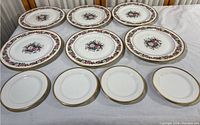 Full view of 10 plates laid out on table; five large floral plates and five smaller plain plates with gold trim