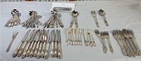 Full set of Oneida White Orchid silver plate flatware laid out on table showing large assortment of spoons, forks, knives, and butter cutting tools.