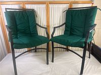 Front view of two matching wrought iron chairs with green cushions, showing overall condition and style.