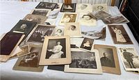 Wide view of various vintage and antique black and white portraits and scene photographs spread on a table showing differences in sizes and cardboard backing on some.