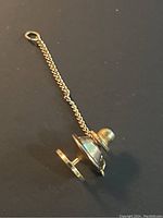 Close-up of the 14K yellow gold tie tack pin with chain showing front side and chain detail on black background.