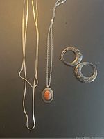 Two sterling silver chains, one pendant with a reddish-orange stone, and two circular sterling silver pendants with engraved floral designs laid flat on dark background.