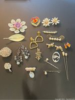 Photo showing full view of the entire collection of vintage brooches, earrings, pins, and hair sticks arranged on flat surface.