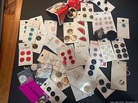 Wide view of collection of vintage buttons on original cards in various colors and styles spread on black surface