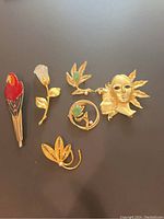 Photo of six vintage costume jewelry brooches arranged on a dark surface showing different designs and materials.