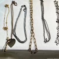 Full view of seven vintage necklaces laid on fabric showing different chain styles and pendants including cross and heart.