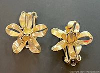 Photo showing rear side of two gold tone flower earrings with clip-on backs, highlighting twisted petal design and construction details.