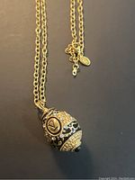 Close-up of Joan Rivers black and gold tone Faberge egg pendant on chain showing pendant detail and chain clasp with tags.