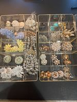 Top view of two divided plastic storage trays containing vintage costume jewelry earrings and some necklaces. Varied styles including floral, rhinestones, pearl-looking beads, turquoise colors, and gold-tone metals.