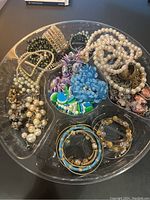 Tray of mixed vintage costume jewelry including pearl necklaces, colorful enamel bangles, floral brooches, and earrings.