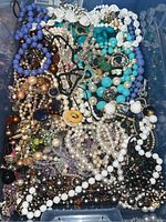 Top view of large mixed collection of vintage costume jewelry in different bead colors and styles laid in plastic bin