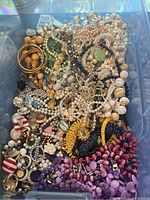 Overhead photo showing a packed box of vintage costume jewelry with necklaces, bracelets, earrings and pins in various colors and materials.