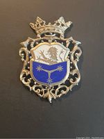 Front view of vintage coat of arms crest showing enameled shield with lion and star motifs, crown top and ornate metal border.