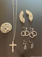 Photo of entire vintage jewelry lot showing round brooch, cross necklace, two pairs of clip-on rhinestone earrings, and one pair of screw-back rhinestone earrings.
