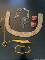 Full view of jewelry collection on black surface showing all items including pearl choker, cross necklace, heart earrings, leaf brooch, heart pendant necklace, and bracelet.