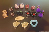 Vintage assorted clip-on earrings and one leaf brooch arranged on black surface, showing variety of shapes, colors, and styles included in lot.