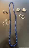 Photo of the lapis lazuli bead necklace and three pairs of clip-on earrings including flower design, small hoops and triangular black stone earrings.