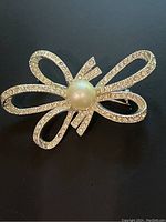 Top view of vintage Richelieu bow pin showing rhinestones and central faux pearl on dark background.