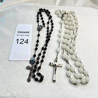 Two vintage rosaries displayed side by side on a white backdrop, one with black faceted beads and the other with white oval beads, showing overall condition and details.