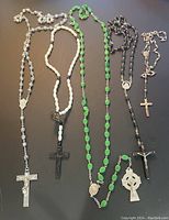 Five vintage rosaries arranged on a flat surface showing different bead colors and crucifix styles.