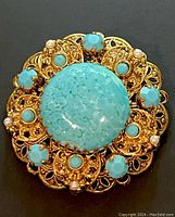 Front view close-up of vintage West Germany brooch pin showing large faux turquoise cabochon center with surrounding smaller turquoise, rhinestones, faux pearls on gold-tone filigree metal base.
