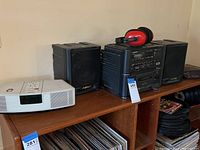 View of Bose Wave Radio, Sharp bookshelf stereo system with two speakers, Sony clock radio and sound control earmuffs displayed on wooden shelving.