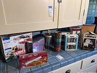 Photo of all boxed kitchen appliances and tools on counter including Sunbeam Food Steamer, Vidalia Chop Wizard, KitchenAid grinder attachment, Cuisinart Mini Chopper, Nutri Slicer