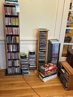 Wide view of several CD and DVD racks with many CDs and DVDs stacked beside them.