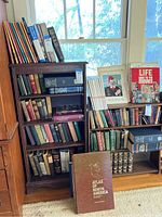 Photo showing a large collection of books on two separate bookshelves, featuring titles including an atlas and assorted older books