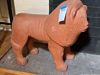 Full side profile of large hollow molded terracotta lion sculpture on tiled floor indoors.