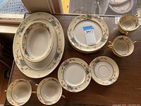 Photo shows assorted plates, cups, and saucers in Lennox Mandolin pattern, arranged on a wooden surface.
