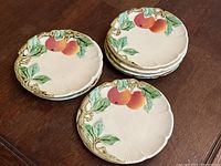 Set of 7 ceramic dessert plates with raised peach and leaf design, shown stacked on a wooden table.