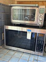 Breville toaster oven stacked on top of stainless steel Kenmore microwave on kitchen counter with tile backsplash.