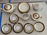 Full set overview showing coffee pot, creamer, sugar bowls, four cups with saucers, and four dessert plates, all decorated with black and gold on white porcelain.