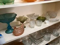 Shelf display of assorted vintage and modern pressed glass items including bowls, dishes, and decorative pieces in various colors and styles.