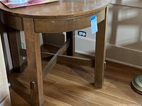 Full view of round top desk table showing sturdy wooden legs and round top surface with wear marks.