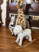 Photo of three large stuffed animals, giraffe in center standing upright approximately 49 inches tall, spotted horse to left, and white rocking cow in front with visible wooden rocker base