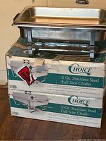 Two stainless steel full size 8 quart buffet chafers on original worn boxes. One chafer shown fully assembled with foldable legs extended; another shown with pans stacked off to one side.