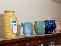 Five vintage ceramic vessels arranged in row on wooden surface showing varied shapes and colors to identify the items in the lot.