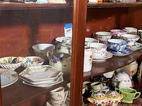 Shelf filled with various vintage china teacups, saucers, and small plates in floral and patterned designs.