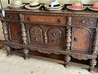 Photo of entire vintage carved wooden buffet from the front, showing intricate carved panels, drawer, cupboard doors, and turned legs.