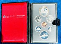 Photo of the opened presentation case showing seven coins mounted in a transparent plastic case: a larger silver dollar and six smaller denomination coins, all proof quality, with red and black case exterior marked Royal Canadian Mint.