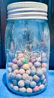 Front view of the glass jar filled with clay marbles showing embossed brand 'THE GEM'.