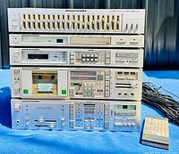 Stack of five Marantz audio components on blue cloth, with remote control and cables beside.