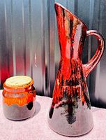 Tall ewer and smaller jar with lava drip glaze photographed against a dark background, showing form and glaze details.